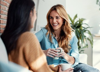 Woman smiling while drinking coffee with friend