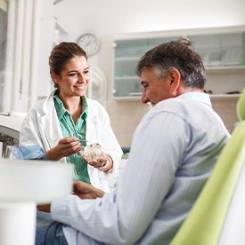 Smiling dentist showing patient model of teeth