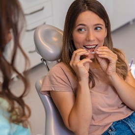 Woman smiling while holding clear aligners in treatment chair